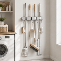 Gray Wall-Mounted Mop & Broom Holder with Hooks gripping mop, broom and dustpan beside a washing machine