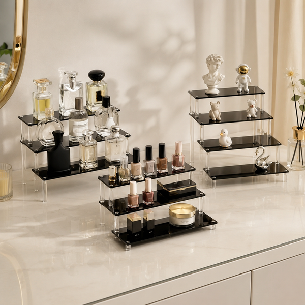 Black tiered acrylic step display risers holding perfume bottles, nail polish, and figurines on a marble vanity