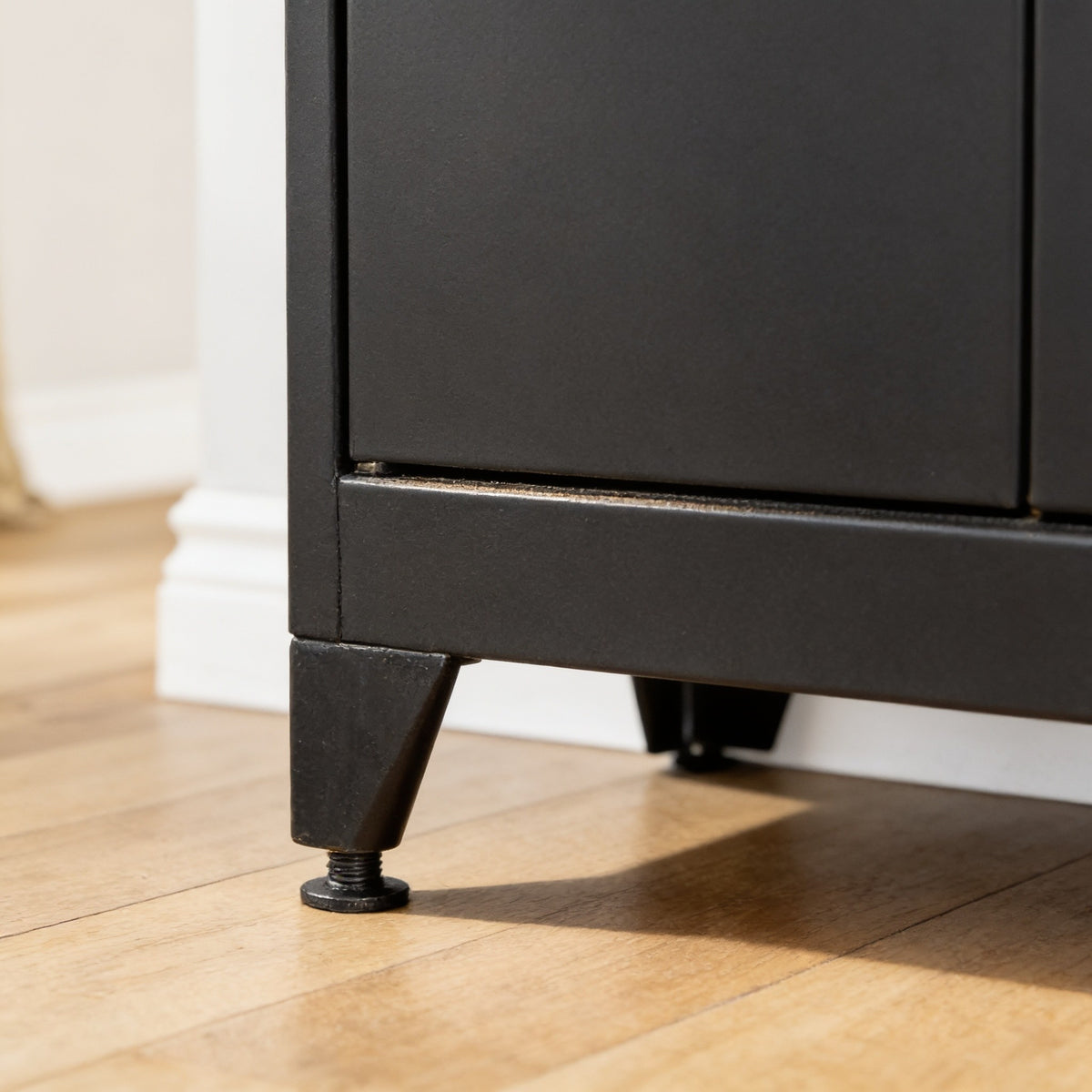 Close low view of one tapered black steel foot lifting the storage cabinet clear of a light oak floor.