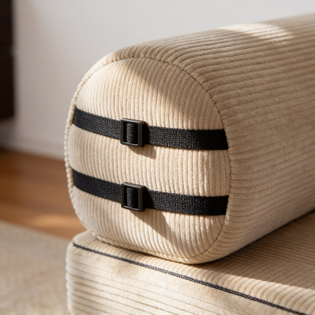 Close view of the sofa's rounded corduroy bolster arm with two black webbing straps and metal buckles.