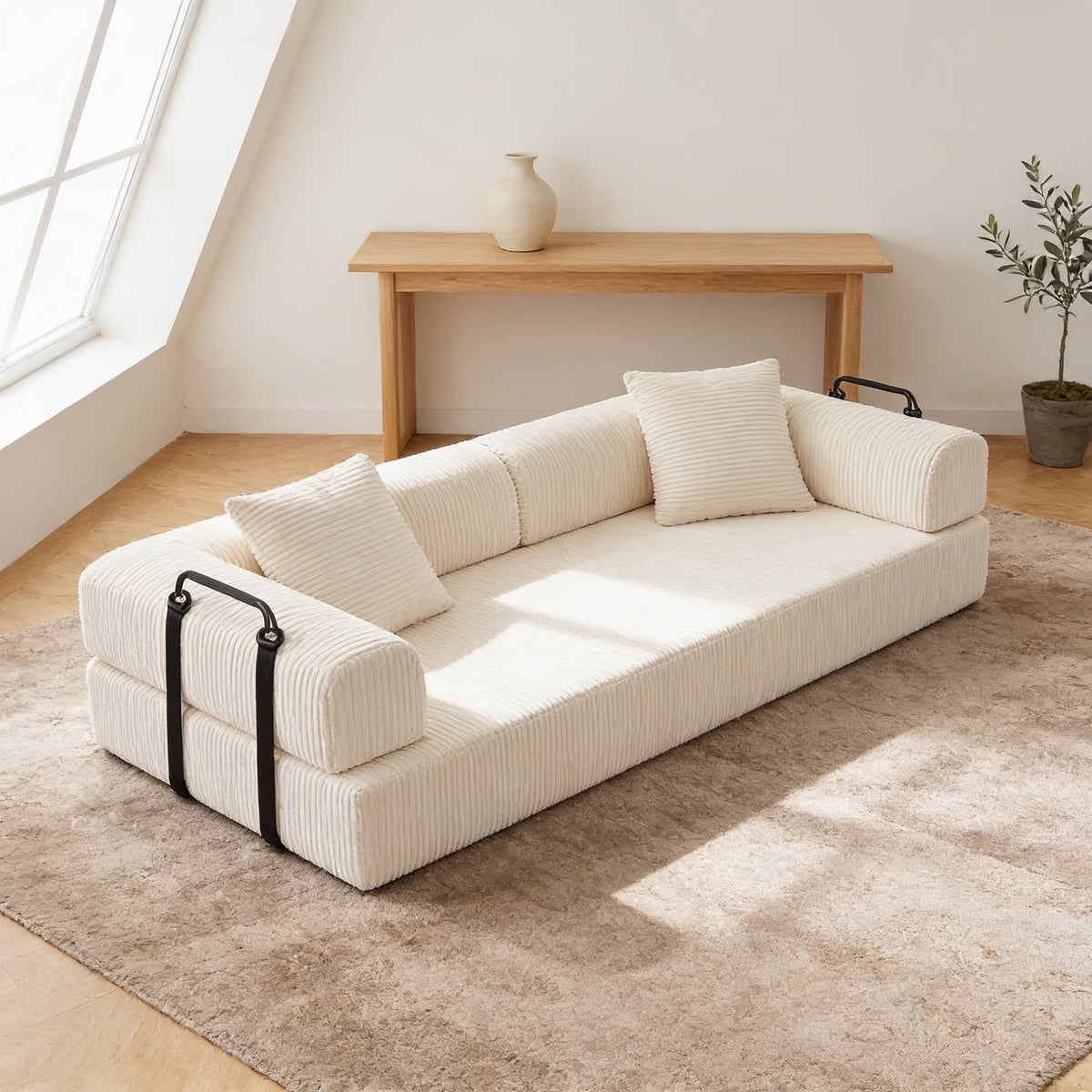 Beige corduroy convertible sofa bed in sofa mode on an oatmeal rug in a warm living room, its low back sitting below the oak console table behind it.