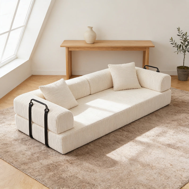 Beige corduroy convertible sofa bed in sofa mode on an oatmeal rug in a warm living room, its low back sitting below the oak console table behind it.