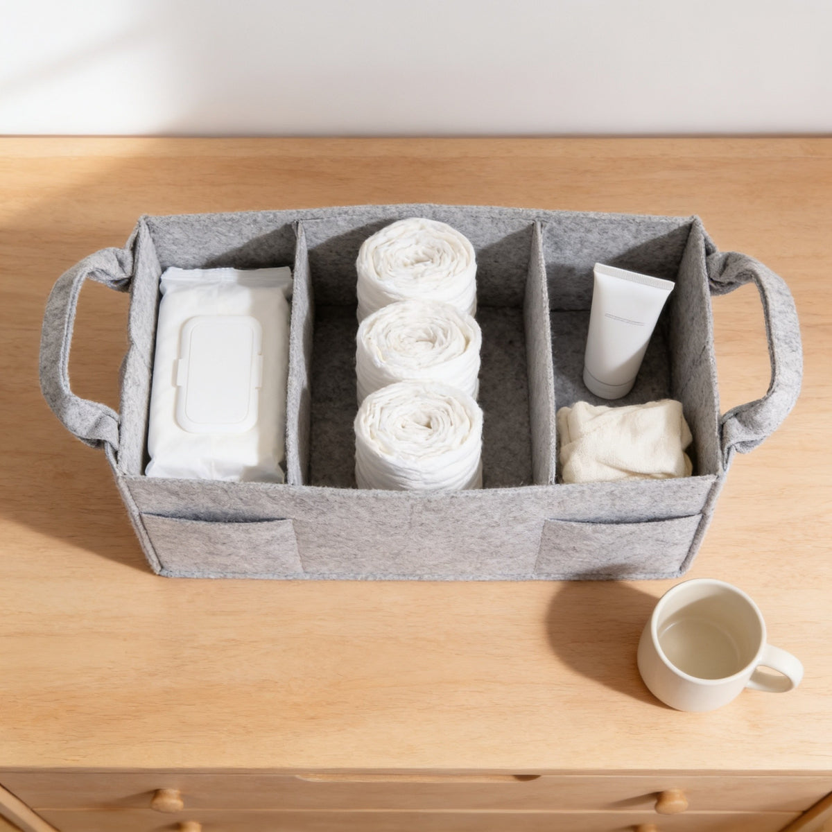 Overhead view of the felt diaper caddy's divided interior beside a mug, showing its 33 by 23 cm footprint.