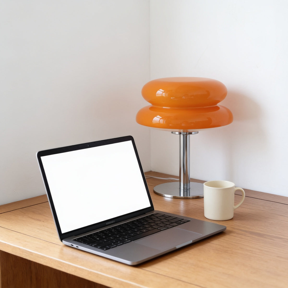 Orange two-tier glass mushroom table lamp on a slim chrome stand beside a laptop and mug on an oak desk.