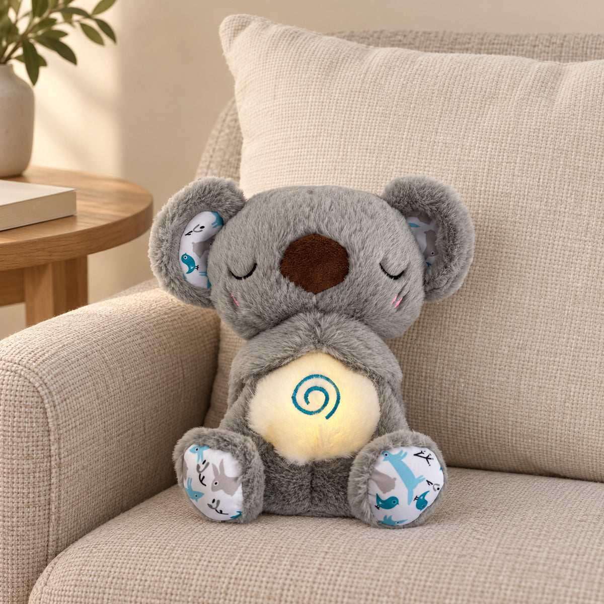 Gray koala breathing plush with a softly lit spiral belly seated on a linen armchair