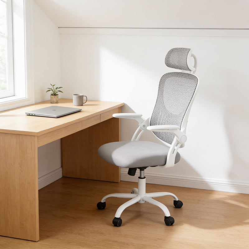 Light gray mesh office chair with adjustable headrest and white frame at a light oak desk in a sunny home office.
