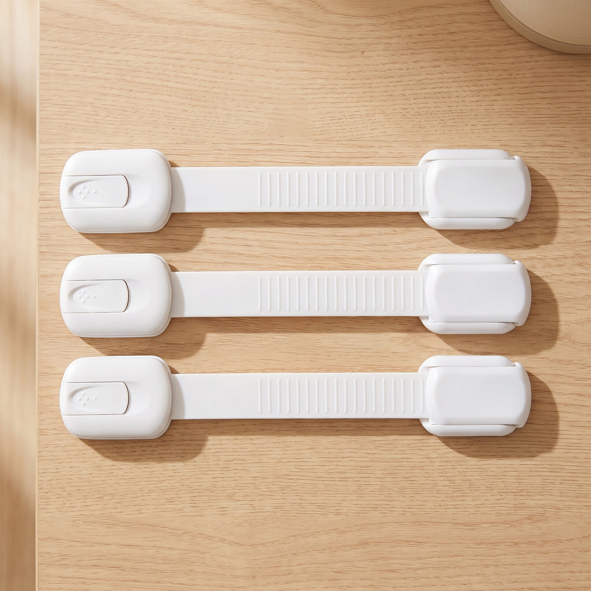 Three white strap cabinet locks on a light oak kitchen countertop