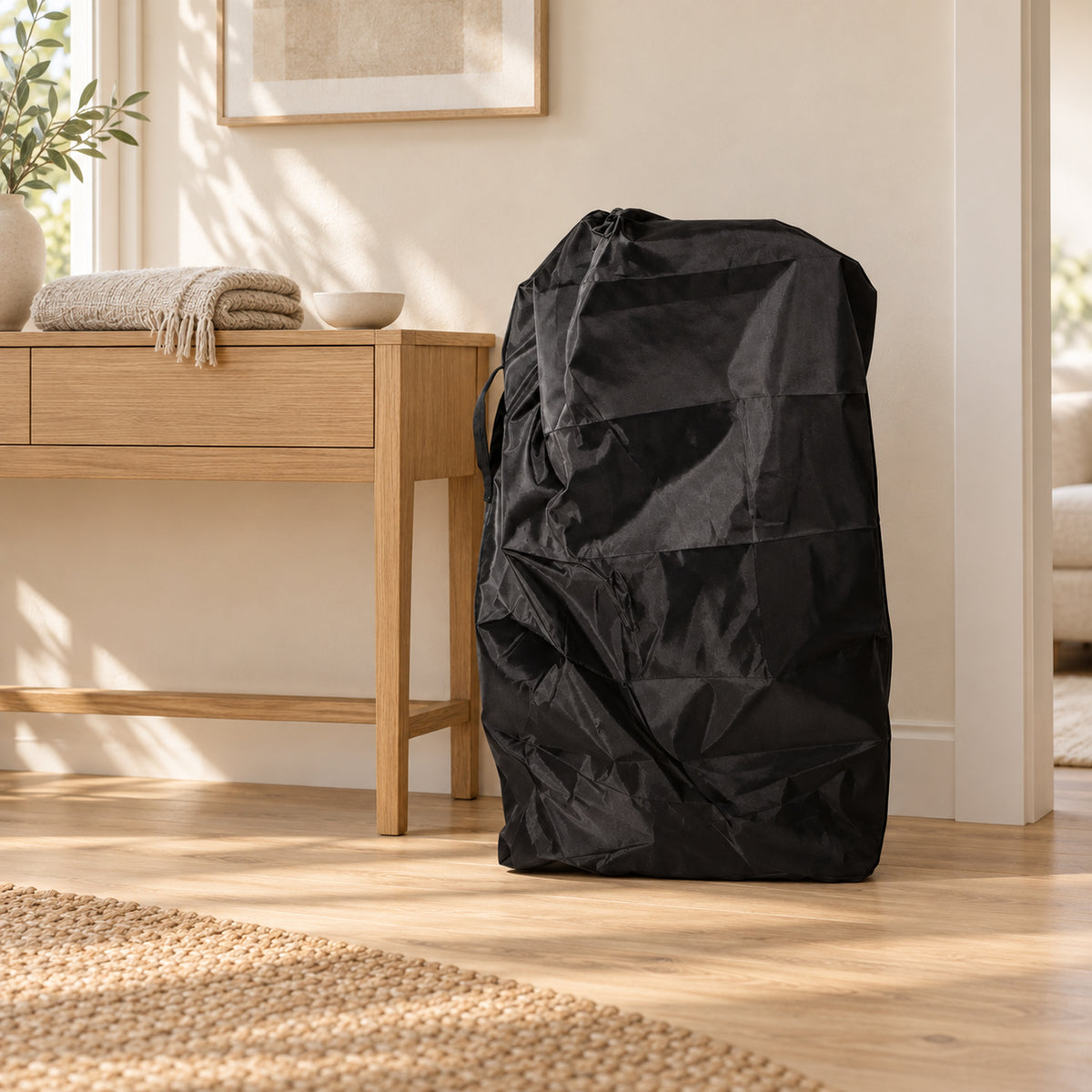 Black stroller travel cover standing beside an oak console in a warm cream living room