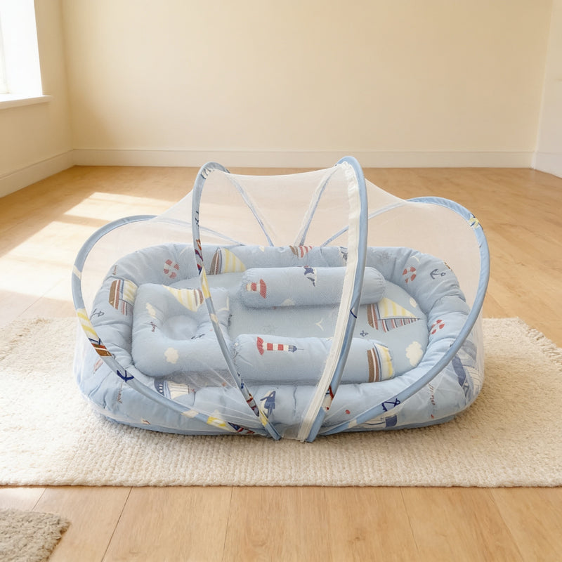 Blue Nautical foldable travel bassinet with sailboat and lighthouse print, white mesh net dome over the padded base, pillow and support rolls, on a cream rug in a bright living room
