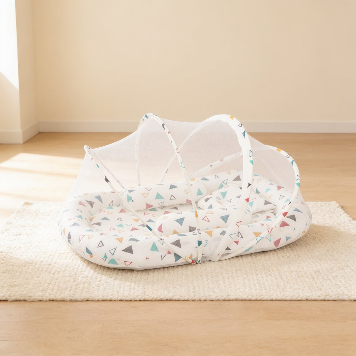 Confetti Triangles foldable travel bassinet, white cotton with scattered coloured triangles, with its mesh net dome up on a cream rug in a bright living room