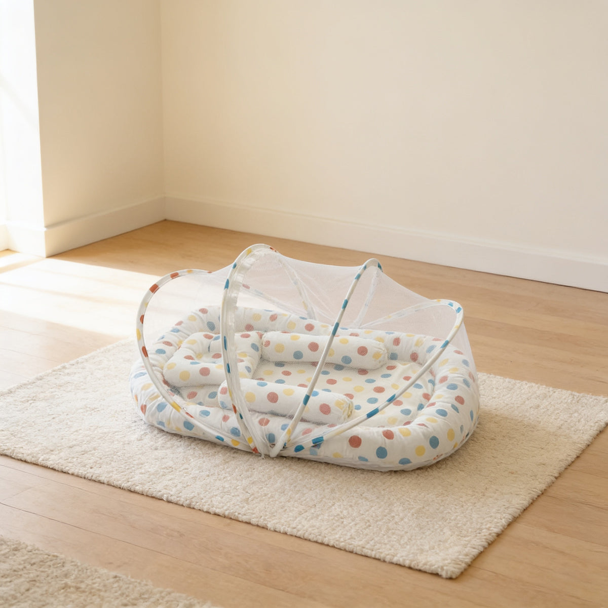 Rainbow Dots foldable travel bassinet, white cotton with large multicoloured dots, with its mesh net dome up on a cream rug in a bright living room