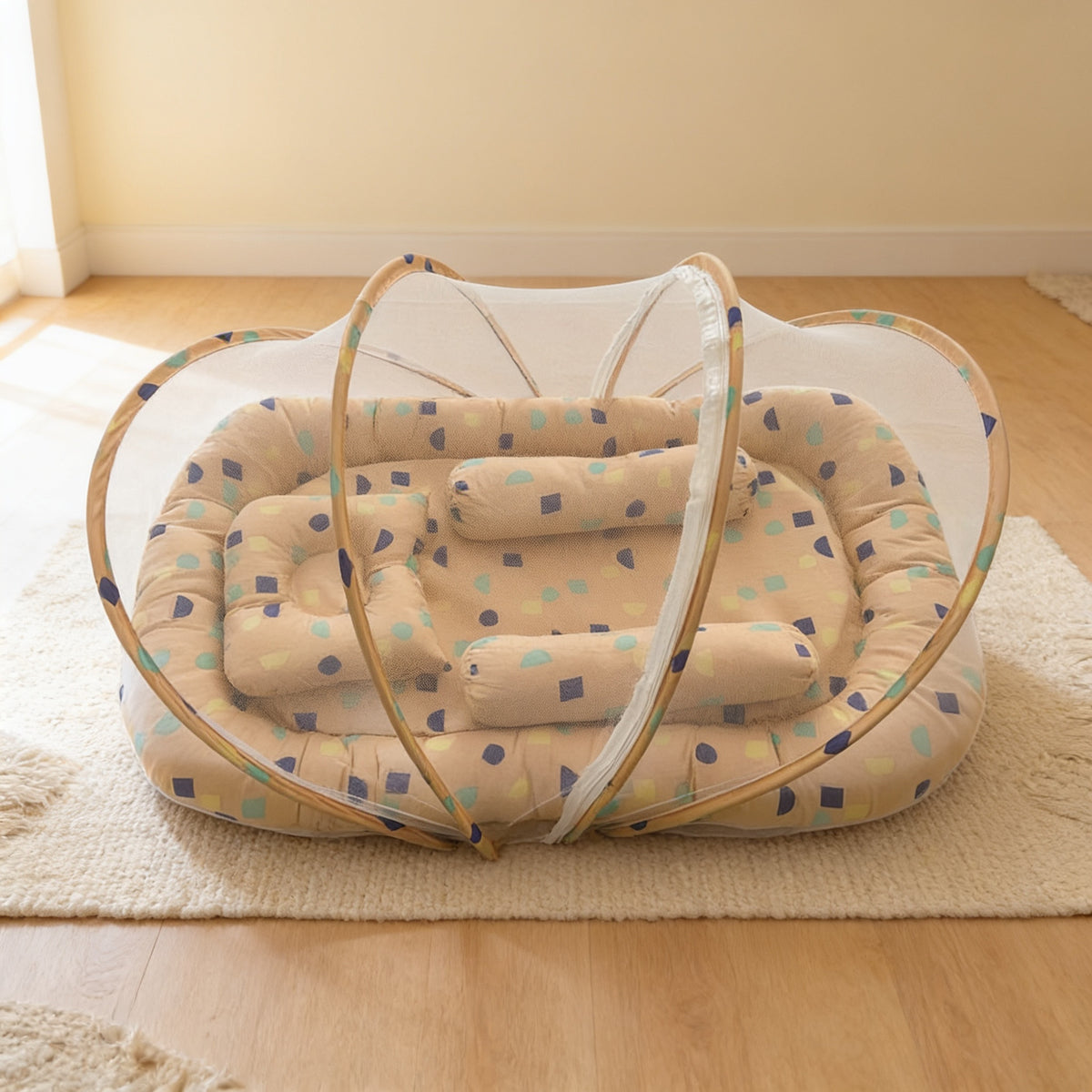Tan Blocks foldable travel bassinet, tan cotton with small coloured squares, with its mesh net dome up on a cream rug in a bright living room