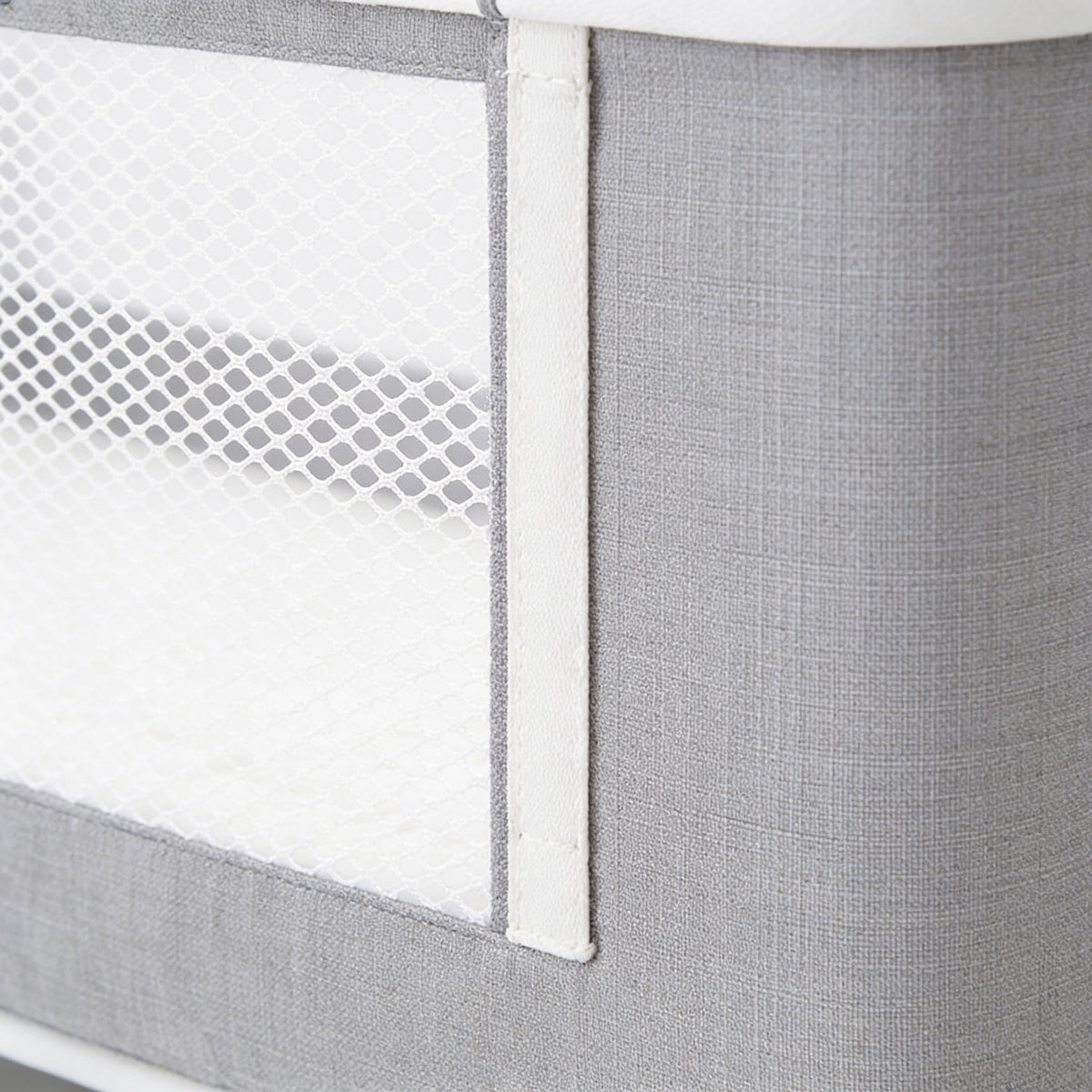 Close view of the white diamond-pattern mesh window set into the fine grey linen-look side wall of the bedside bassinet, with its flat white binding strip and straight stitching