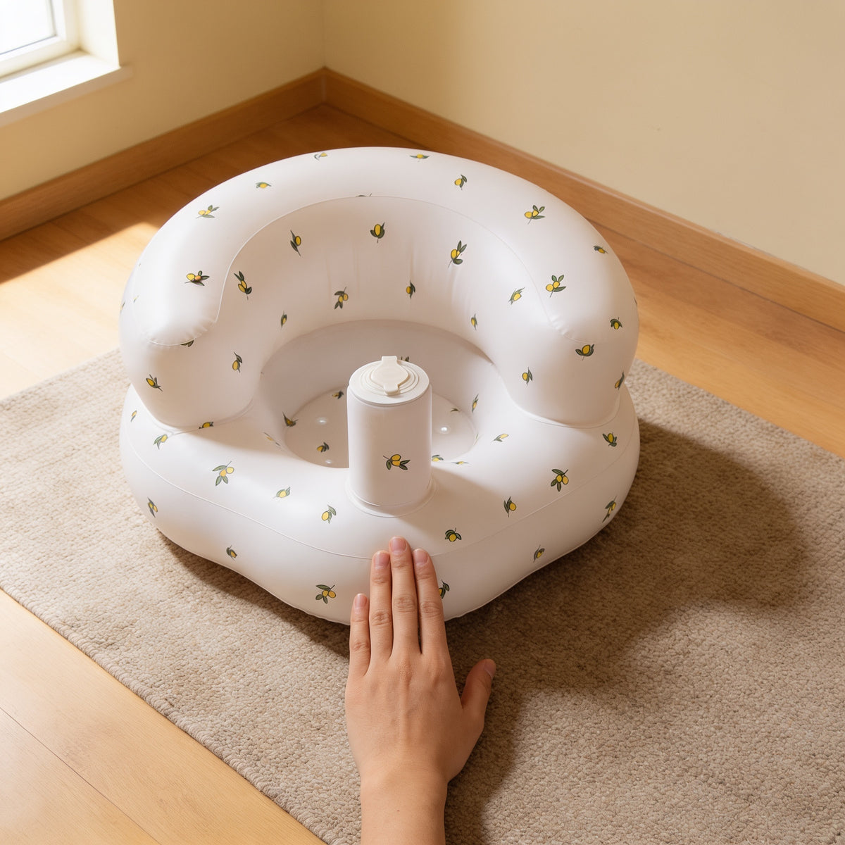Olive Flower inflatable baby floor seat on a woven rug with one adult hand laid flat in front of it for scale, showing the seat is about six hand-widths across
