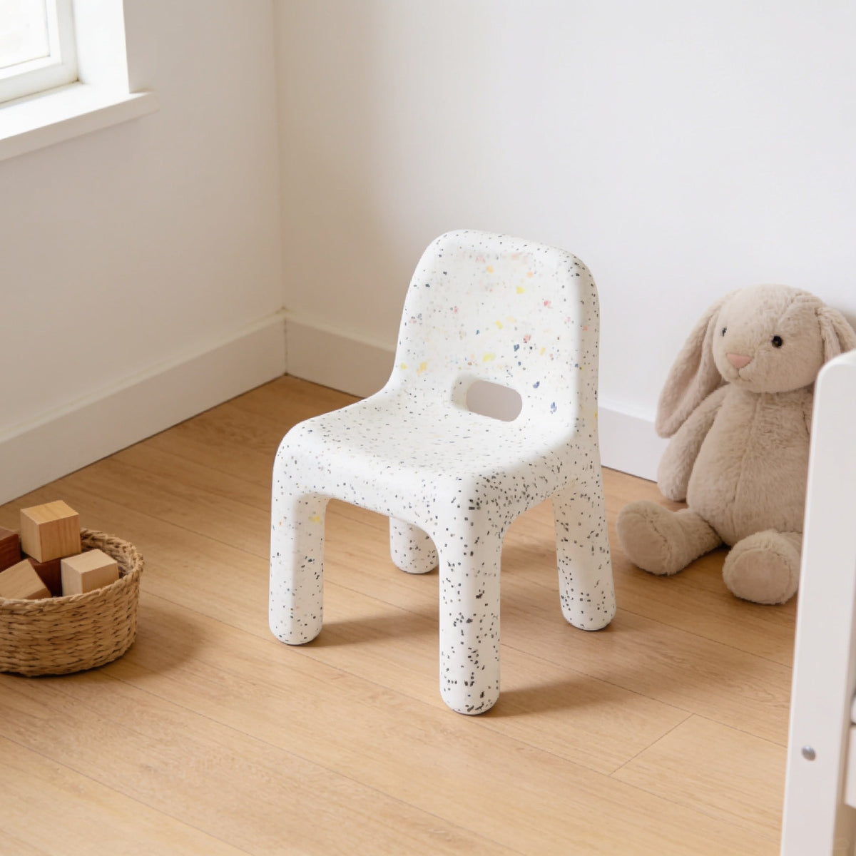 Spotted speckled molded kids chair with a hand-hole backrest in a sunny kids room.