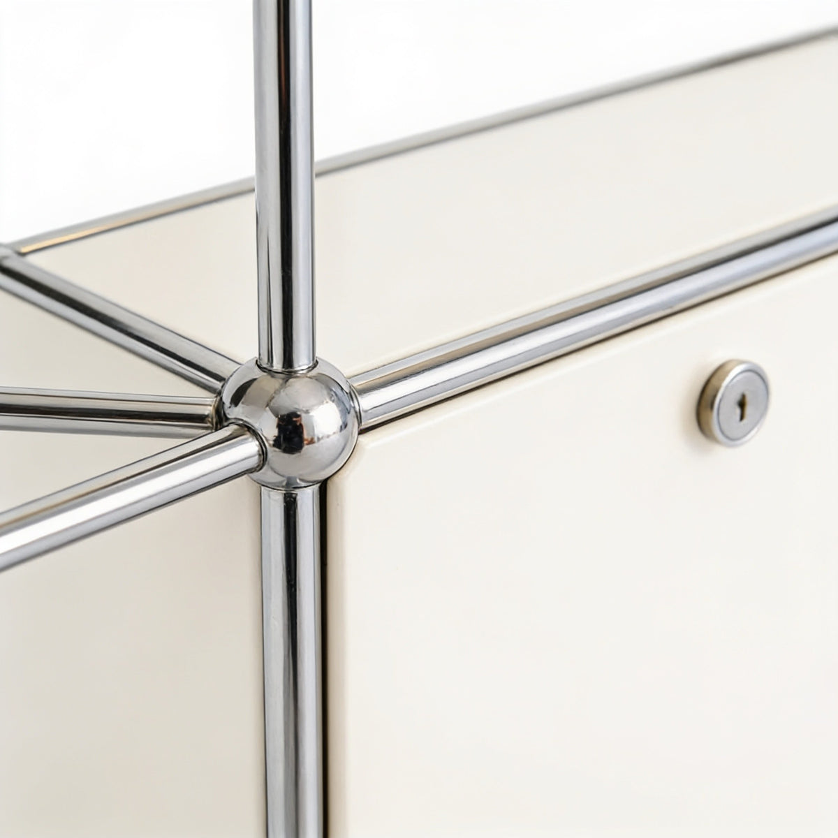 Close detail of a polished chrome ball connector joining the frame tubes beside a white steel door with its lock.