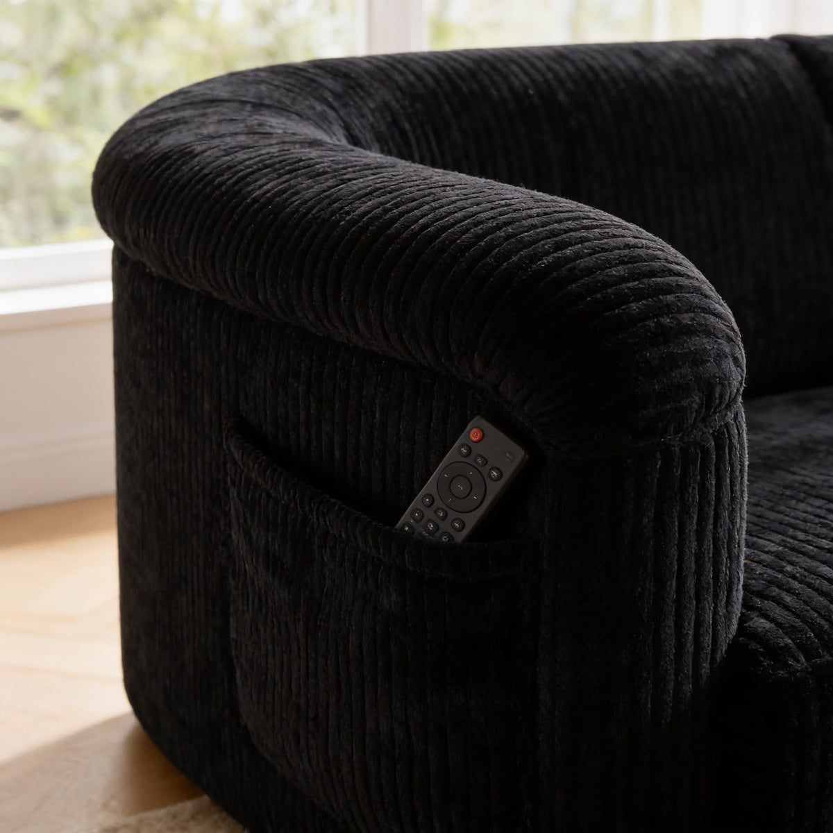 Close detail of the black wide-wale corduroy arm with a remote in the side pocket.