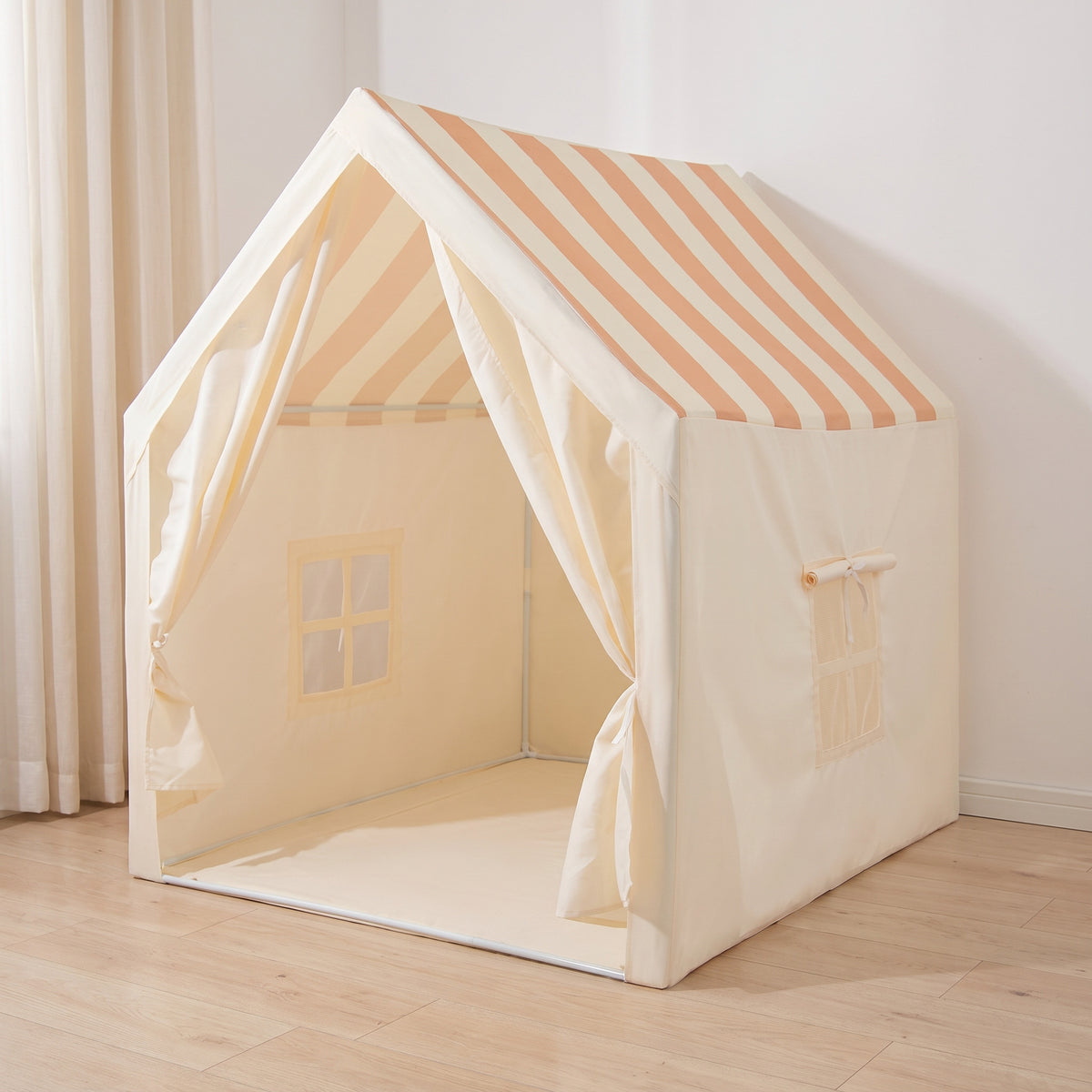 Cream house-shaped kids play tent with a peach striped roof in a bedroom corner, curtain doors tied back