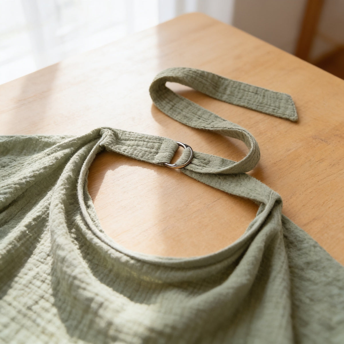 Close-up of the muslin nursing cover neck strap threaded through its metal D-ring.