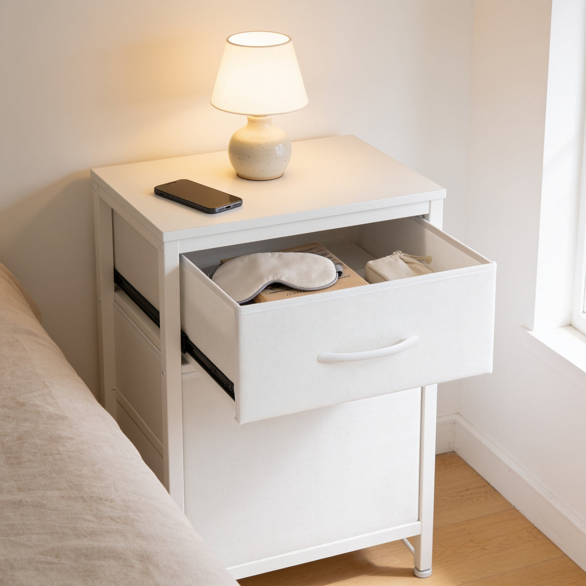 Upper fabric drawer of the nightstand pulled open with a sleep mask and book inside.