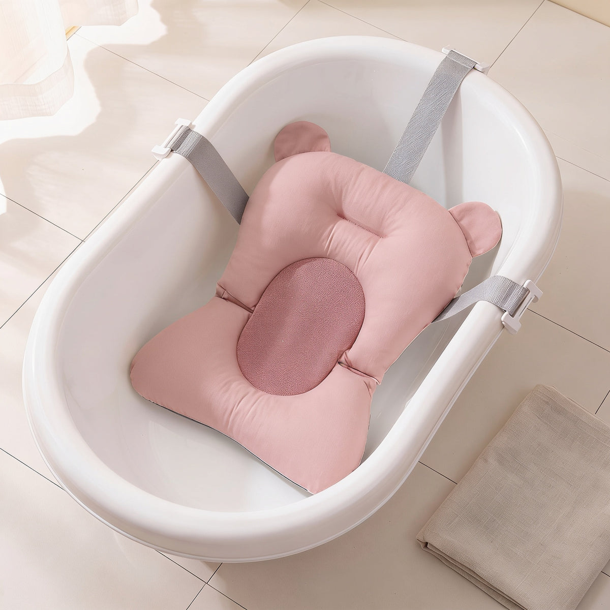 Pink non-slip newborn baby bath cushion with a deeper pink mesh centre, fitted in the same empty white baby bathtub with its belts clipped over the rim