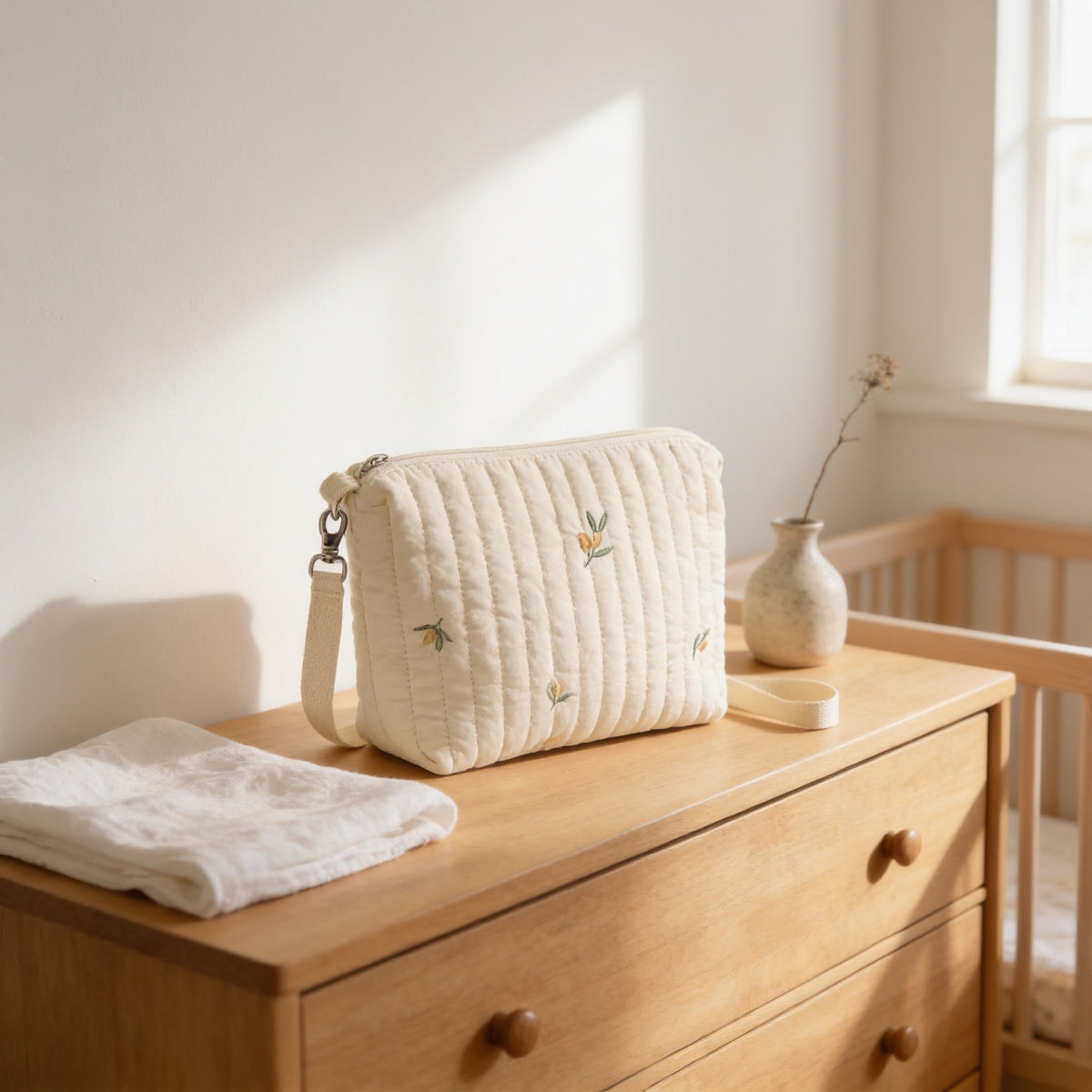 Quilted diaper pouch with embroidered olive sprigs on a nursery dresser, 25 cm wide.