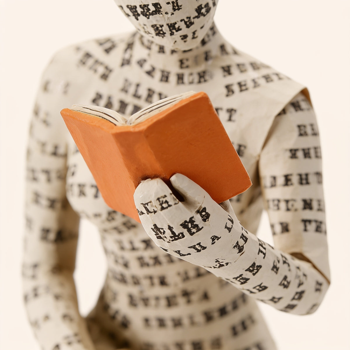 Close-up of the printed-letter paper texture and orange book — Paper-Pulp Reading Figurine