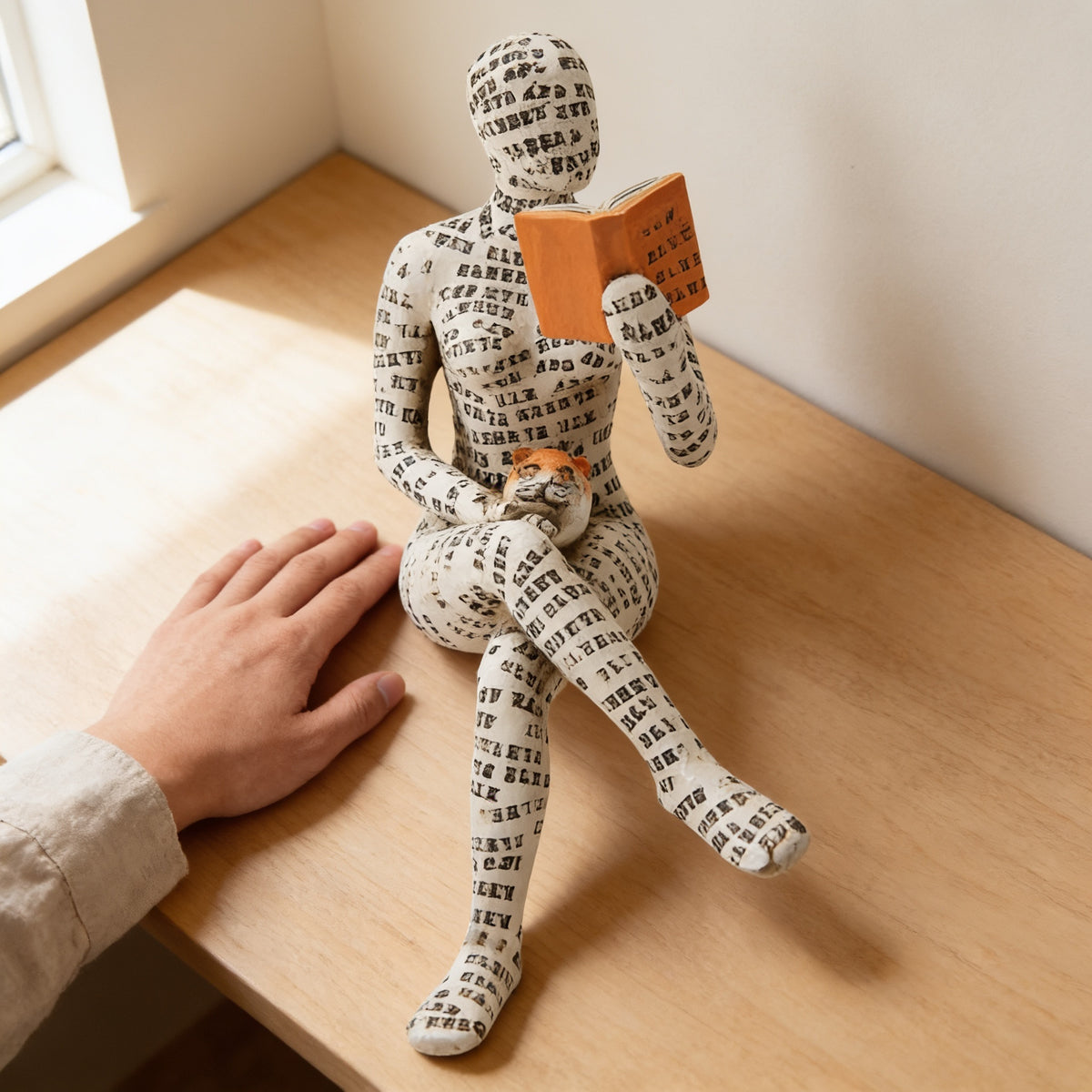 Paper-pulp reading figurine on an oak table next to a hand for scale — Paper-Pulp Reading Figurine