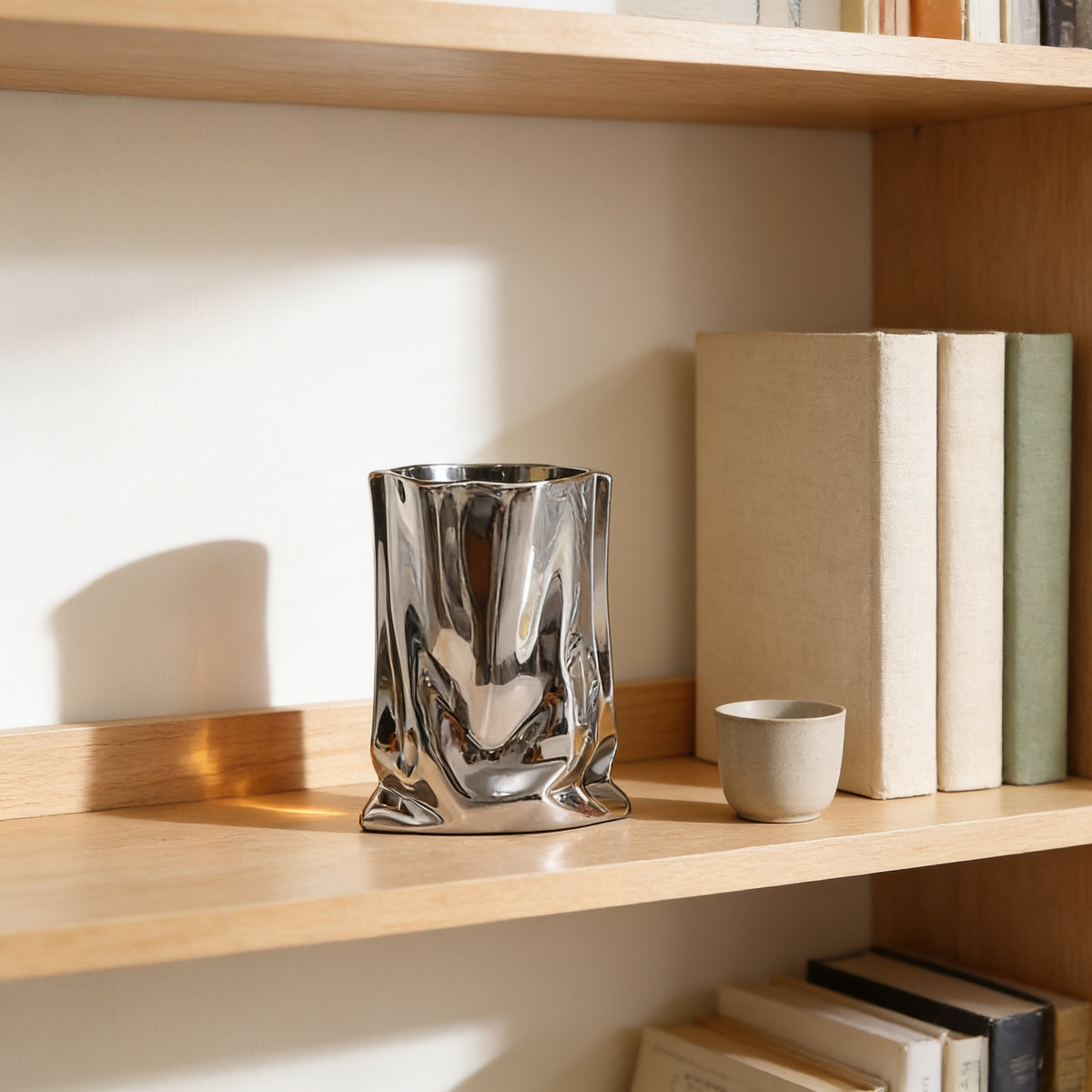 Silver crinkle vase shown empty on an oak bookshelf beside books — Silver Crinkle Paper-Bag Vase