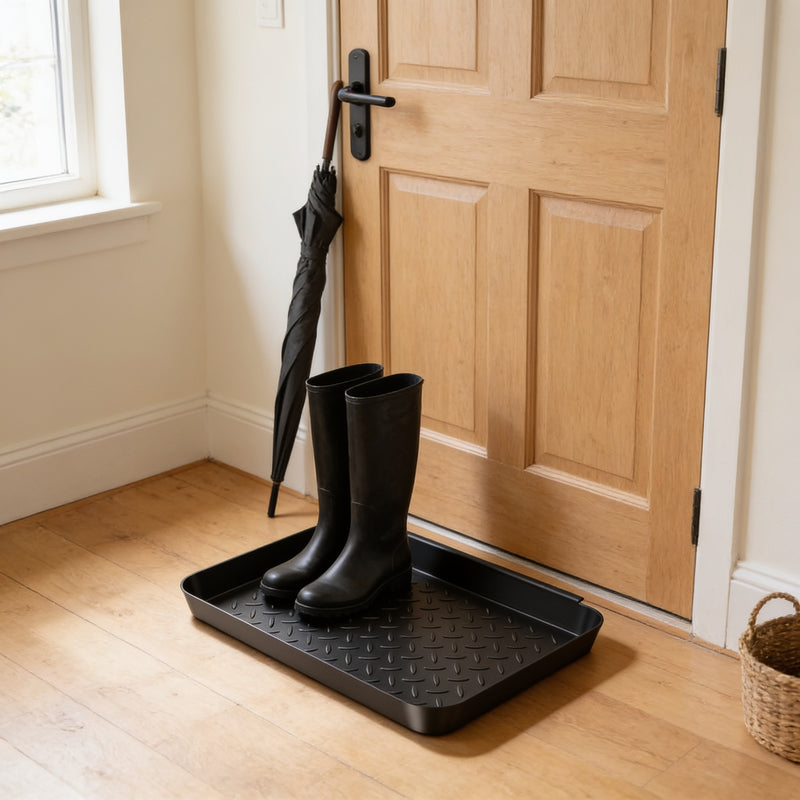 Textured black boot tray with wet boots and umbrella by a front door