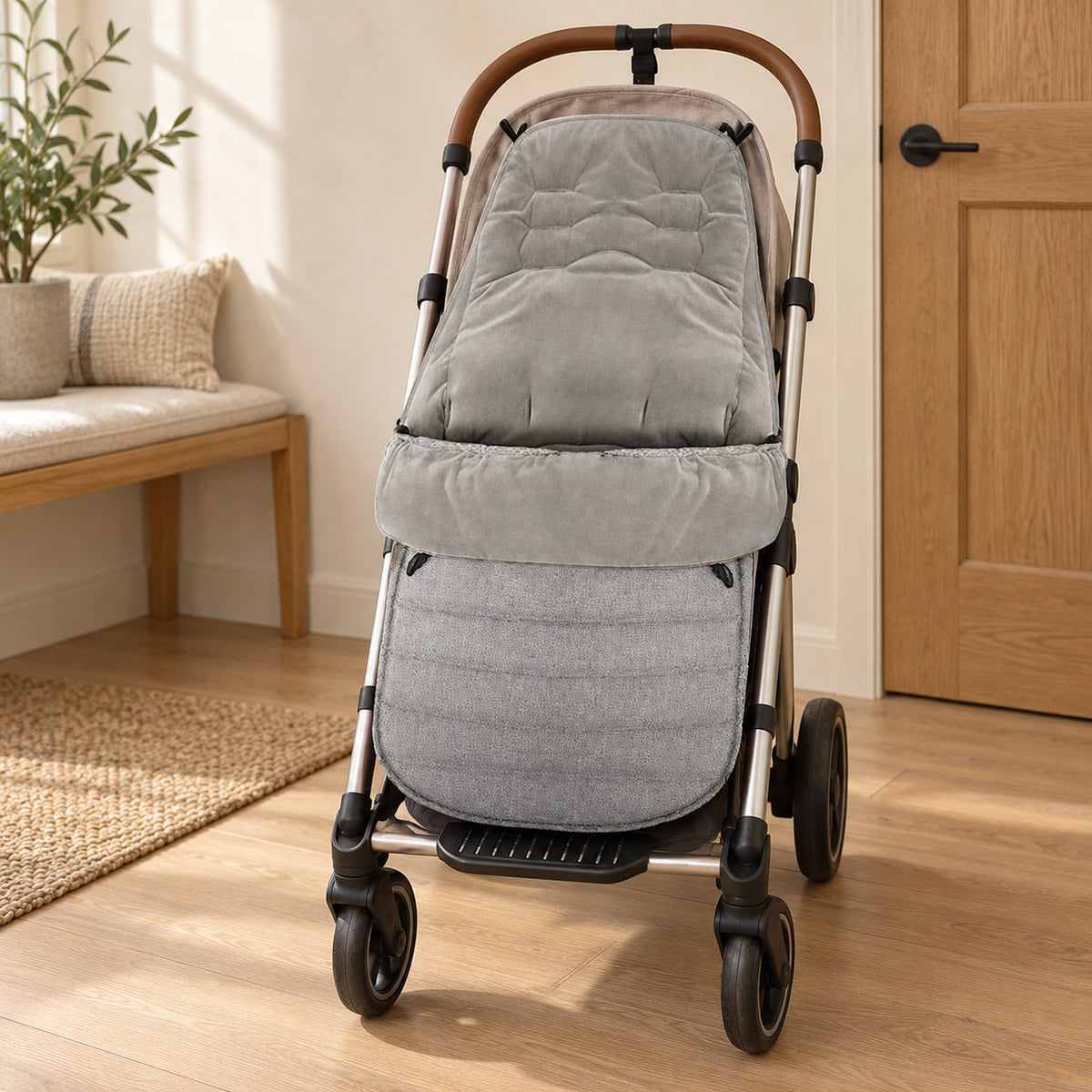 Gray velvet-lined stroller footmuff on an empty stroller beside an oak bench in a warm entryway