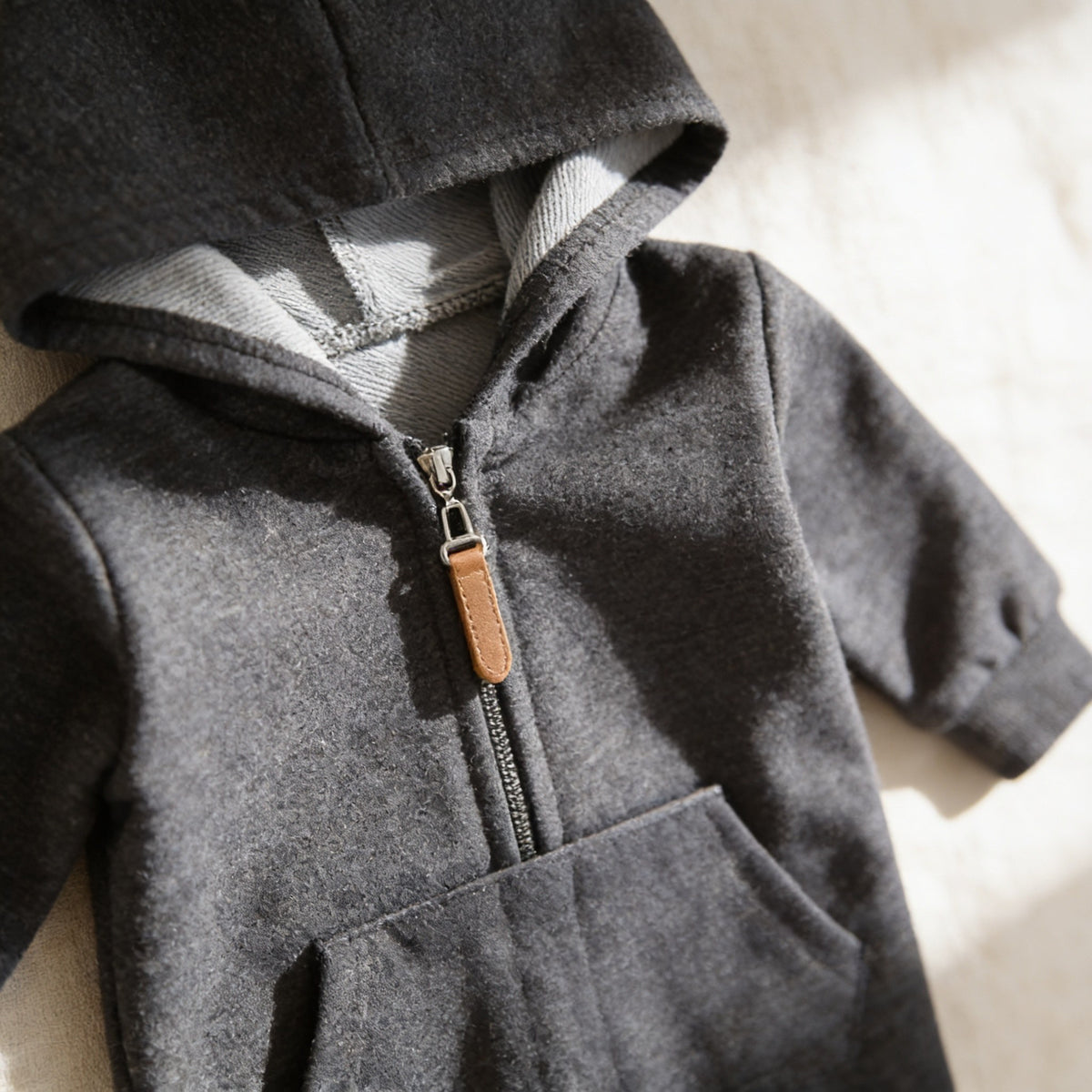 Close detail of the romper's heather-lined hood, front zip and tan zip pull.