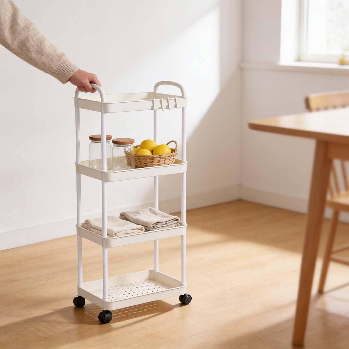 Hand pushing the white four-tier rolling utility cart across an oak kitchen floor by its arched handle.