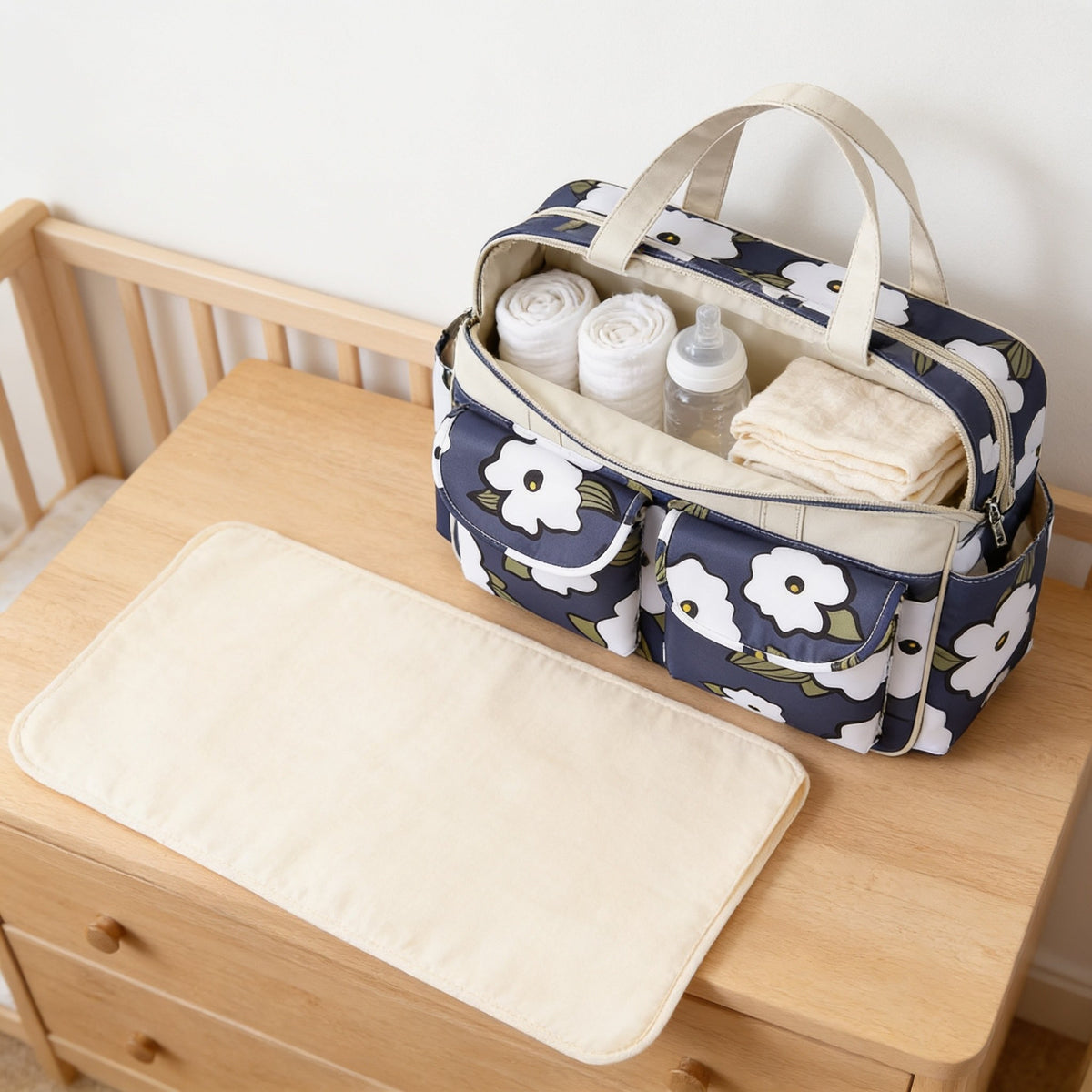 Open diaper tote holding nappies, a bottle and muslin, with its changing mat unfolded in front.