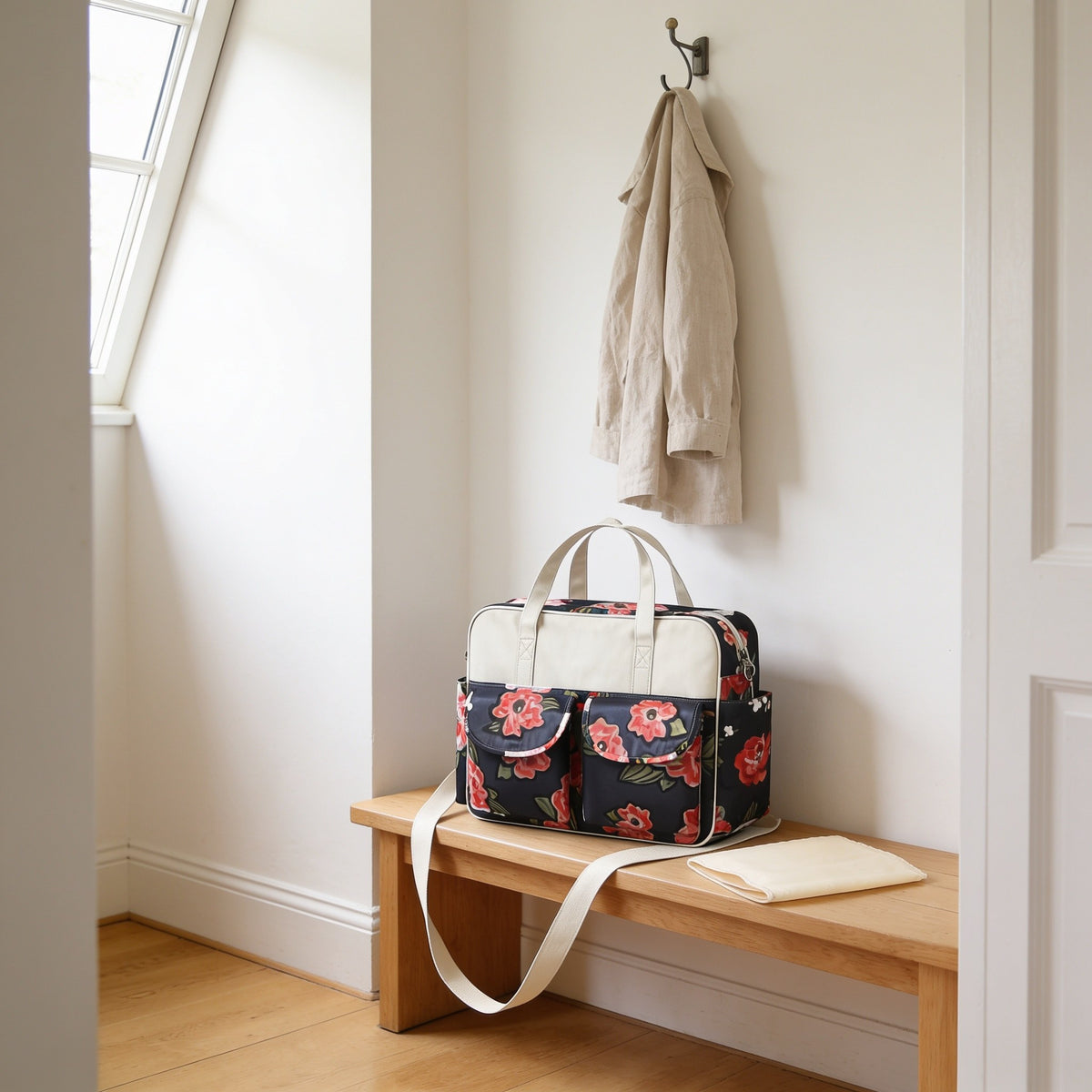 Black rose print diaper tote bag on a light oak hallway bench, its changing mat folded beside it.