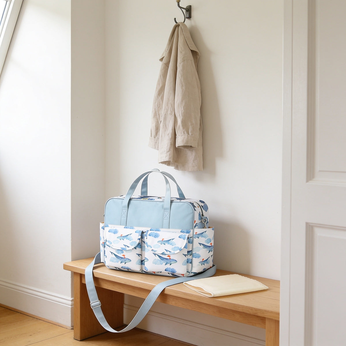 Blue whale print diaper tote bag on a light oak hallway bench, its changing mat folded beside it.