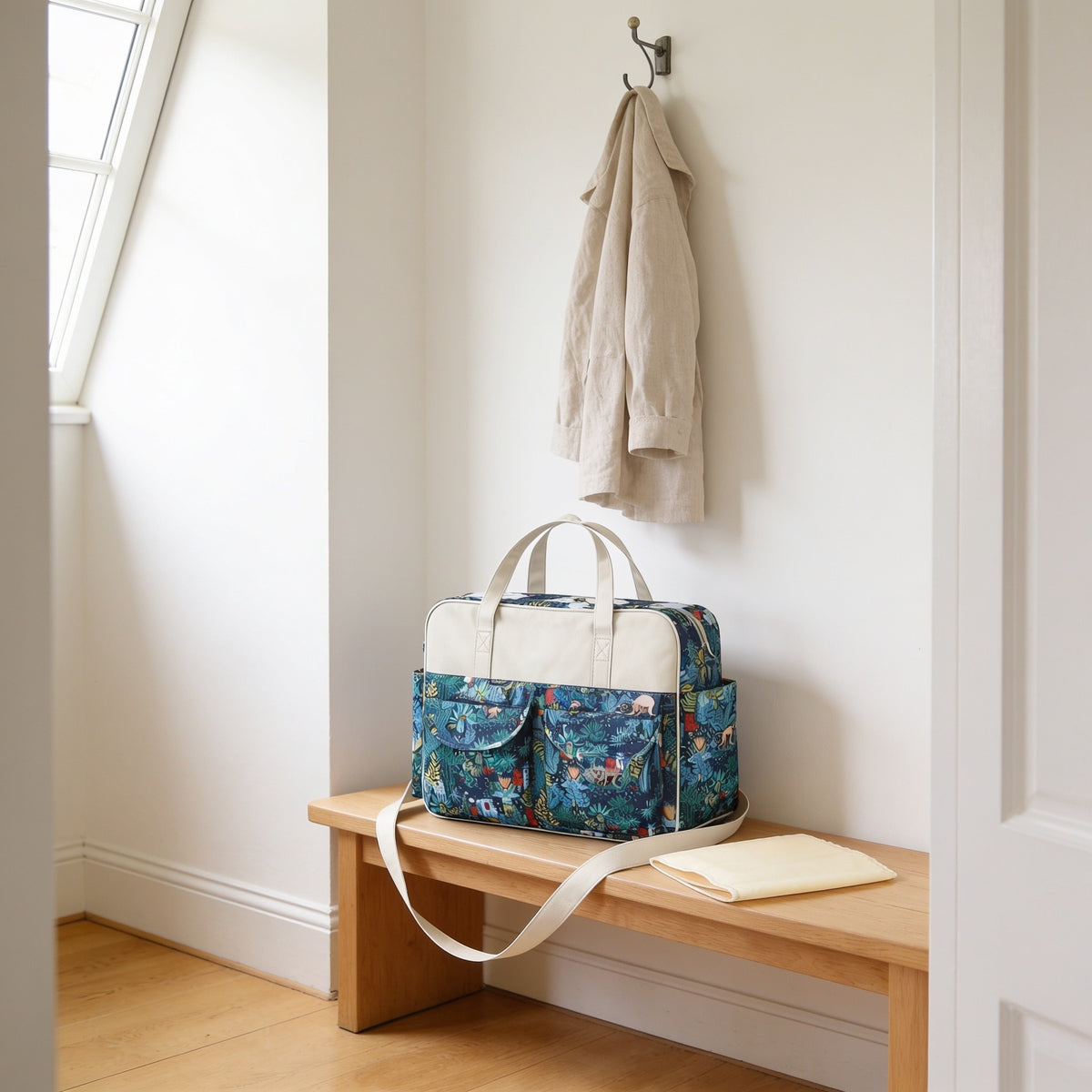 Teal jungle monkey print diaper tote bag on a light oak hallway bench, its changing mat folded beside it.