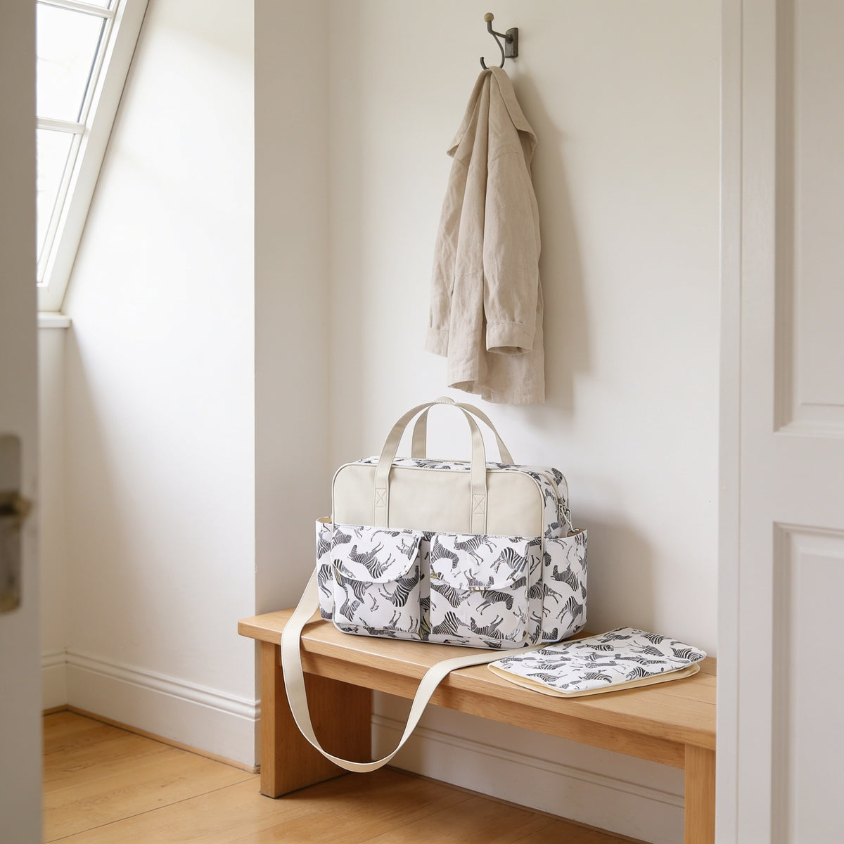 Zebra print diaper tote bag on a light oak hallway bench, its changing mat folded beside it.