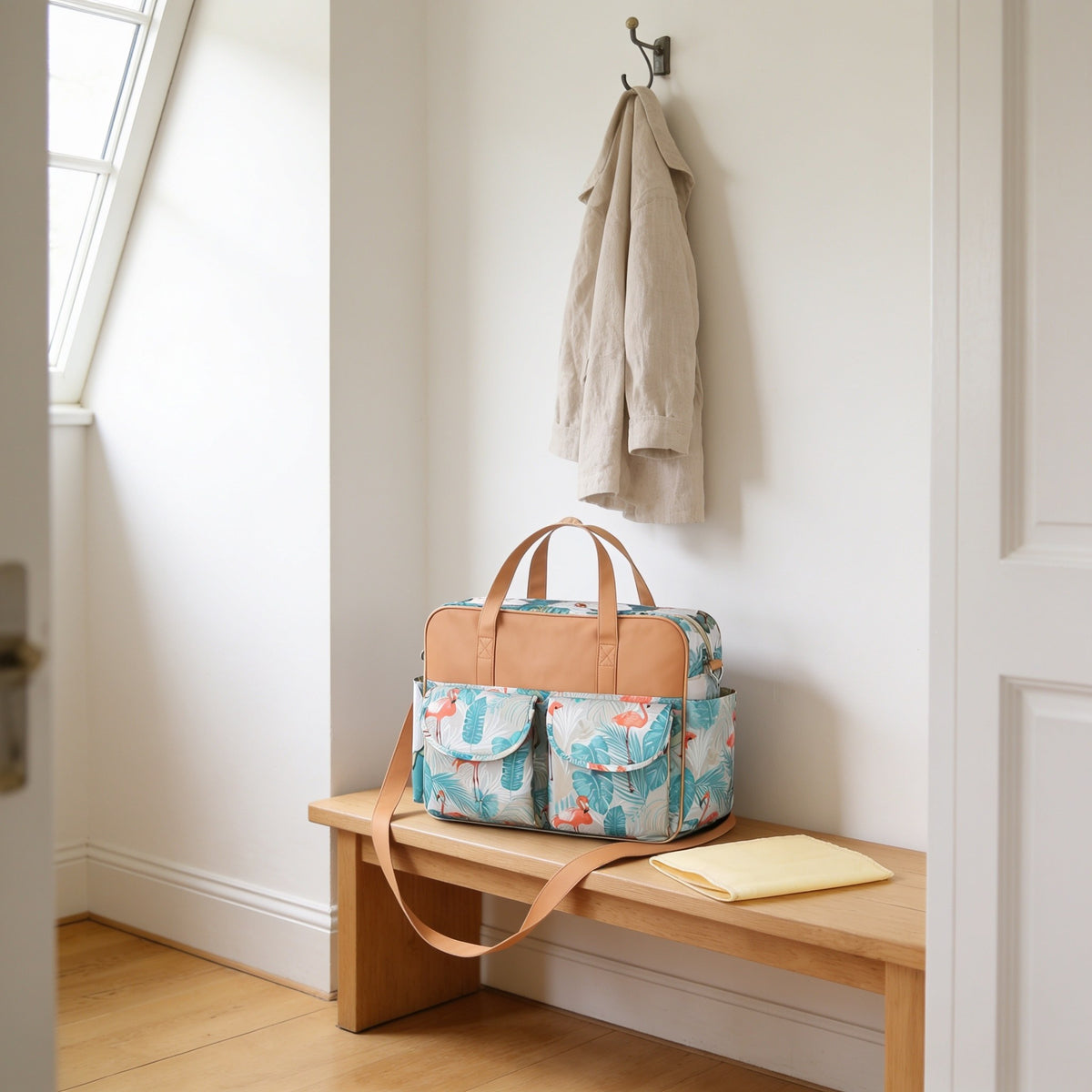 Teal flamingo print diaper tote bag on a light oak hallway bench, its changing mat folded beside it.
