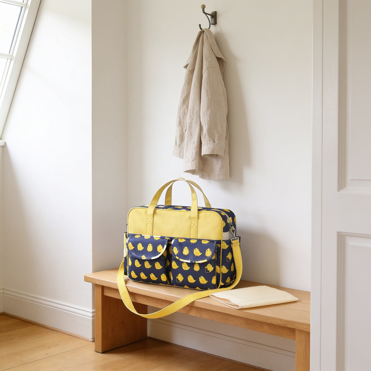 Navy chick print diaper tote bag on a light oak hallway bench, its changing mat folded beside it.