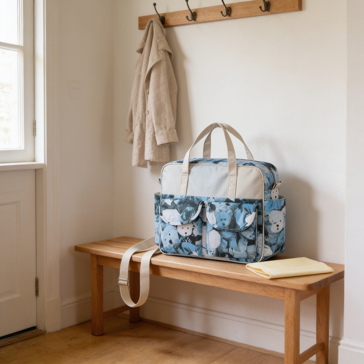 Blue teddy bear print diaper tote bag on a light oak hallway bench, its changing mat folded beside it.