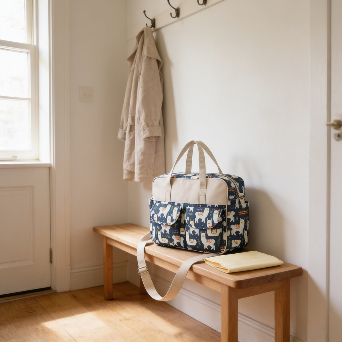 Navy alpaca print diaper tote bag on a light oak hallway bench, its changing mat folded beside it.