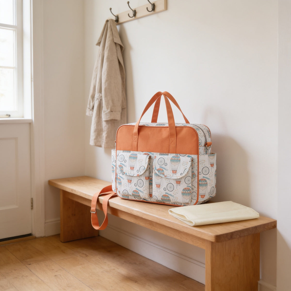 Hot air balloon print diaper tote bag on a light oak hallway bench, its changing mat folded beside it.