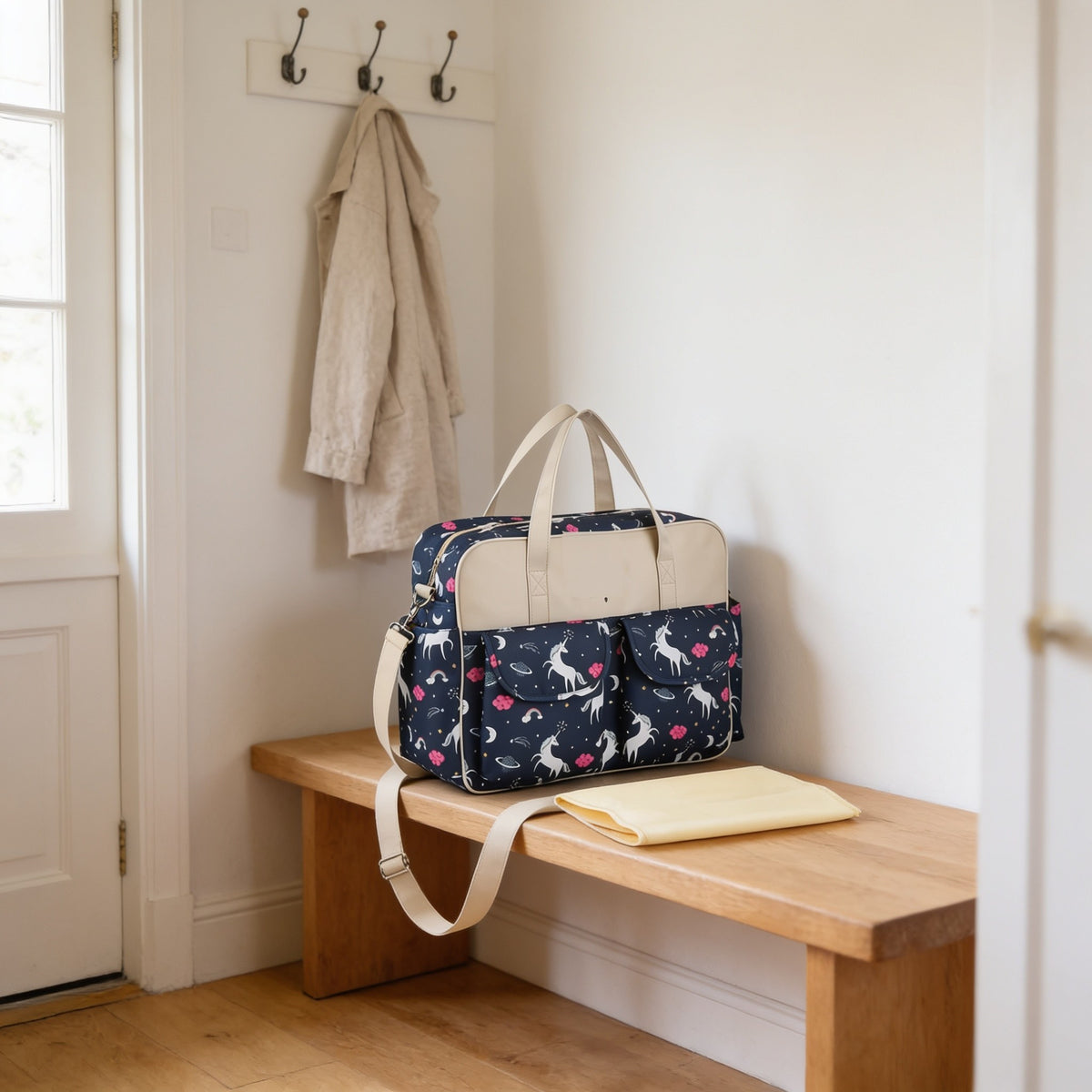 Navy unicorn print diaper tote bag on a light oak hallway bench, its changing mat folded beside it.