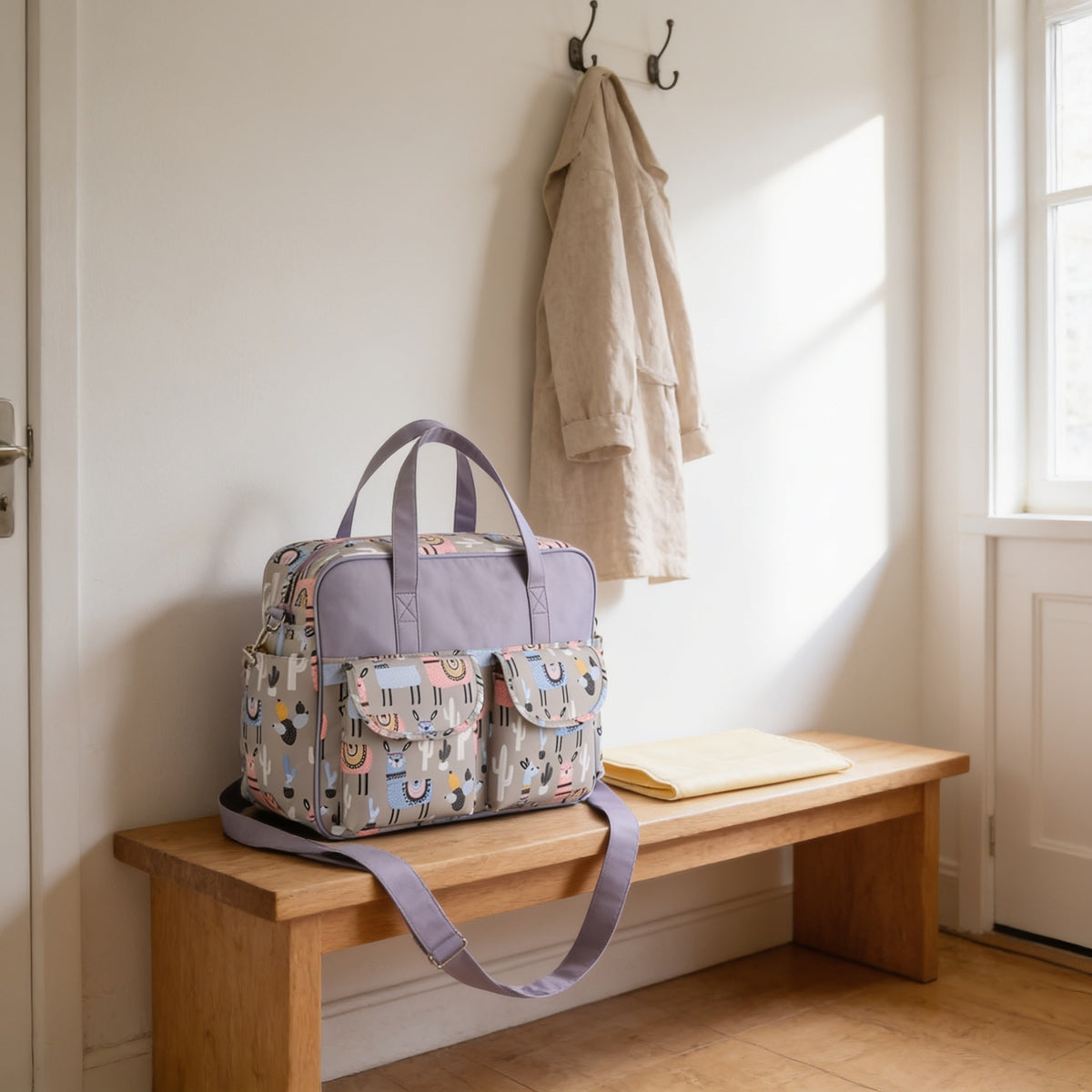 Gray alpaca print diaper tote bag on a light oak hallway bench, its changing mat folded beside it.