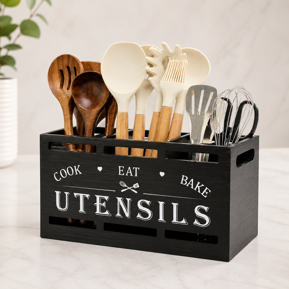 Black wooden utensil caddy printed with Cook Eat Bake holding wooden spoons, whisks, and spatulas