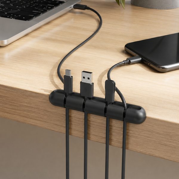 Black adhesive cable organizer clip on a desk edge holding four charging cables in separate slots