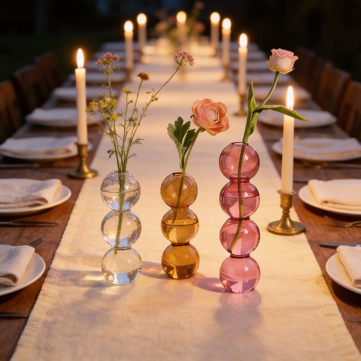 Clear, amber and pink bubble vases down the centre of a candlelit dinner table.