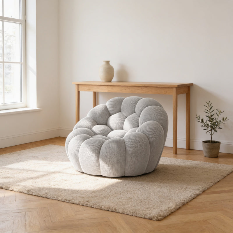 Light grey bubble armchair in a three-dimensional mesh knit, sitting directly on an oatmeal rug in a warm living room.