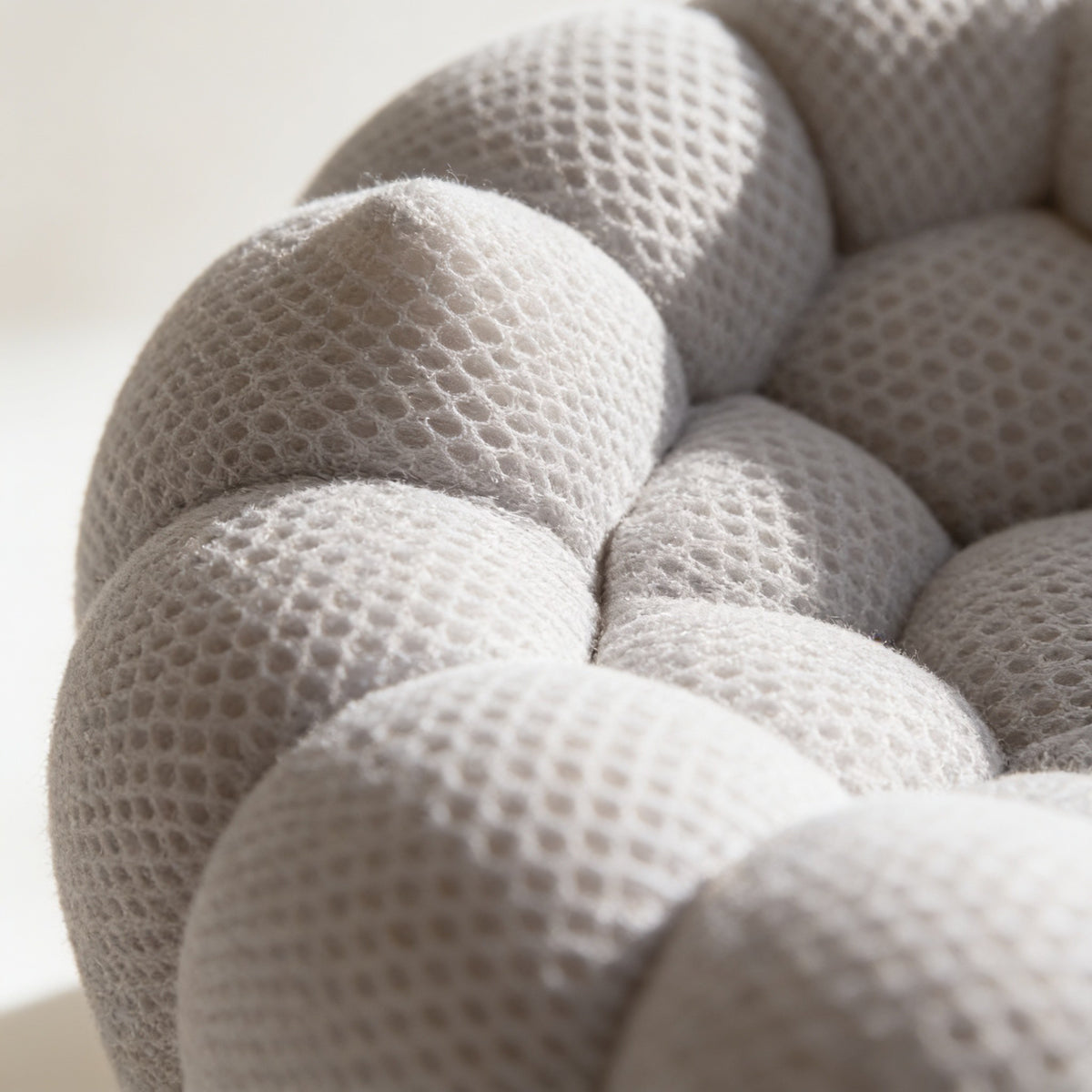 Macro detail of the three-dimensional honeycomb mesh knit stretched over the rounded bubbles of the chair.